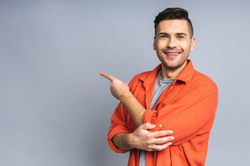 Look over there! Happy young handsome man in casual pointing away at copyspace and smiling while standing isolated over white grey background.