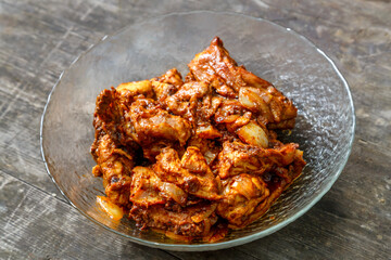 Pieces of chicken in sauce fried in a glass plate on a dark wooden table.