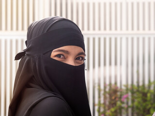 Close up of pretty muslim woman covering her face while outdoors. Gorgeous woman wearing black...