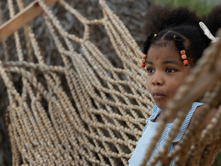 Close up, portrait of pretty little African girl feeling excited while sitting on rope hammock. Copy space to use..