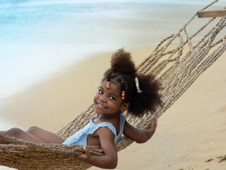 Pretty little African girl relaxing in the rope hammock on the beach. Summer vacation holiday concept.