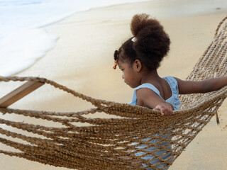 Pretty little African girl relaxing in the robe hammock on the beach. Summer vacation holiday...