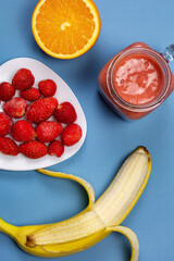 Fruits and berries on a bright blue background. A set of banana, orange and strawberry for making a pink smoothie. Red smoothie recipe with a selection of fresh ingredients.