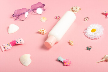 Children's sunscreen, sunglasses accessories and jewelry on a pink background. Cosmetics and accessories for little girls, flat lay. Summer baby cosmetics
