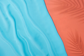 Creative flat lay with blue silk fabric and tropical leaves shadows on pastel pink background. Minimal summer concept.