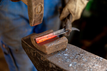 Close up view of heated metal and anvil. The blacksmith in the production process of metal products handmade in the forge. Blacksmith forging metal with a hammer. Metal industry, old profession.