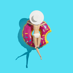 Creative flat lay with girl in bikini sunbathing by summer donut inflatable toy in swimming pool. Minimal summer holiday concept background. Tropical party idea.