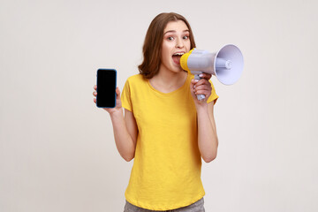 Young attractive woman wearing yellow T-shirt holding megaphone and showing black screen of mobile...