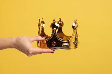 Closeup of woman hand holding golden crown, concept of awards ceremony, privileged status, superior...