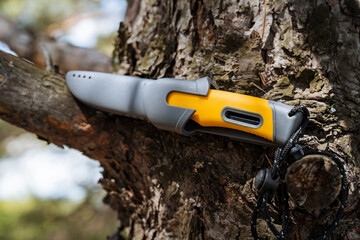 Bushcraft knife on the background of the bark of the tree, camping equipment hiking knife for cutting bread, yellow handle, gray sheath, plastic cover.