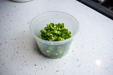 View of coloful diced jalapeno peppers in a plastic container on a kitchen counter, prepped for cooking