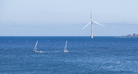 Two small lateen sailboats sail near an offshore wind turbine on the island of Gran Canaria