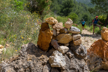 Stones piled up on a rock, in a natural setting, with hikers out of focus in the background.