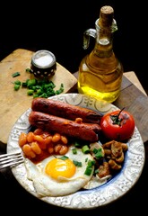 breakfastt with fried eggs, sausages, bacon, beans and mushrooms. Dark wooden background. top view