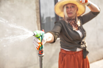 senior female gardener 60 years old  in abandoned backyard. Blond serene woman working planting flowers in garden at summer time. Gardening, hobby, leisure concept.