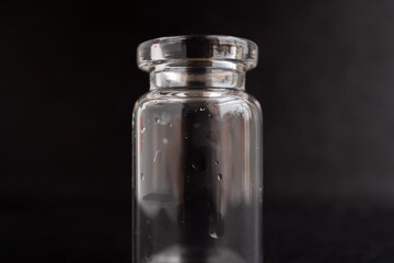 Close up de una botellita de cristal o vidrio vacía sobre fondo negro con un poco de humedad