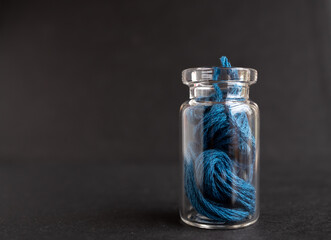 botellita de vidrio llena con madeja de hilo de algodón azul para bordar y fondo negro