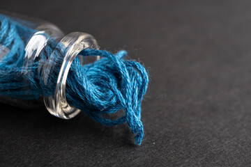 botellita de vidrio llena acostada con madeja de hilo de algodón azul para bordar y fondo negro...