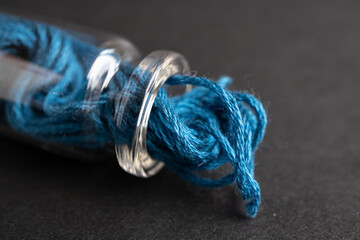 botellita de vidrio acostada llena con madeja de hilo de algodón azul para bordar y fondo negro