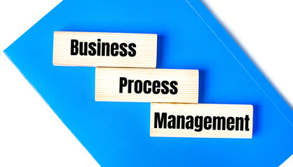 There is a blue notebook on a light gray background. Above are three wooden blocks with the words BPM Business Process Management