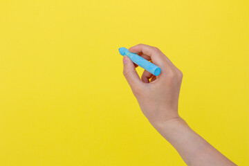 Hand holding blue chalk isolated on yellow background.