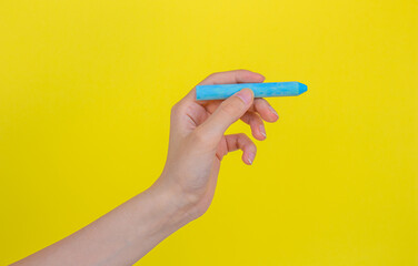 Fototapeta na wymiar Hand holding blue chalk isolated on yellow background.