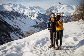 A loving couple plays together in the snow outdoors. Winter holidays in the mountains. Man and woman in knitted clothes have fun on weekends.