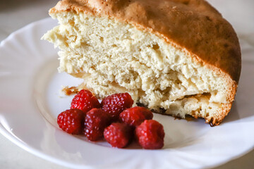 Piece of the homemade apple pie on the white plate served with some raspberries