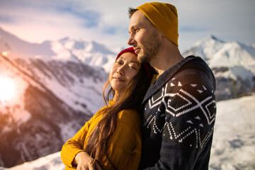 A loving couple plays together in the snow outdoors. Winter holidays in the mountains. Man and woman in knitted clothes have fun on weekends.
