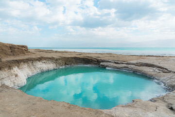 Sinkhole filled with turquoise water, near Dead Sea coastline. Hole formed when underground salt is...