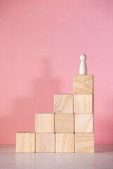 Piece of wood in the shape of a person on a podium and a pink background