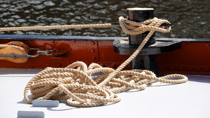 A pile of rope on the deck of a ship. It's tied to a bollard. It's connected with a wooden pulley.