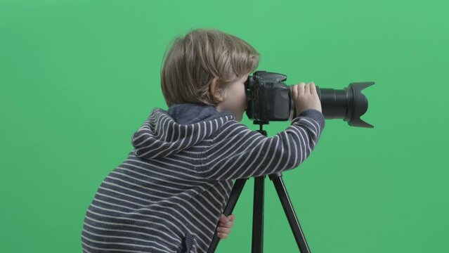 Little child blonde hair play with  photo camera, serious boy zoom, green screen background