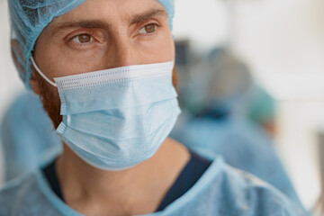 Fototapeta na wymiar Close up of professional doctor in mask standing in operating room before surgery and looking away
