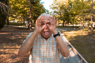 Hombre mayor con gesto divertido y con la lengua fuera, en el parque. Fotografía horizontal.
