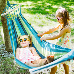Happy childhood. Five year old girls ride on a hammock in the garden. Sunny summer weather. Square photography.