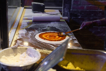 The process of making pizza. Skilled chef in apron preparing ,adding, applying tomato sauce on the dough and mozzarella cheese and pizza dough rolling with hands. 