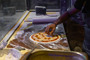 The process of making pizza. Skilled chef in apron preparing ,adding, applying tomato sauce on the dough and mozzarella cheese and pizza dough rolling with hands. 