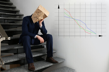 Man wearing paper bag with drawn sad face indoors and illustration of falling down chart. Economy...