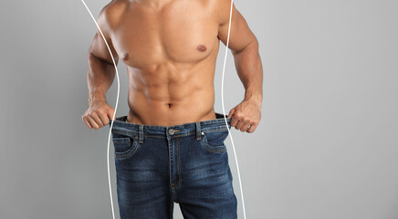 Closeup view of man with muscular body in oversized jeans on grey background, space for text....