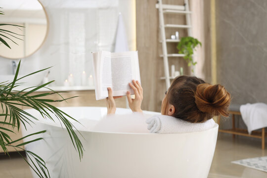 Woman reading book while enjoying bubble bath at home