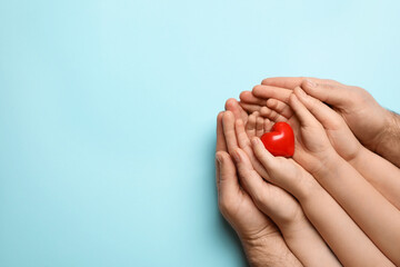 Parents and kid holding red heart in hands on light blue background, top view. Space for text