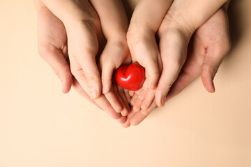 Parents and kid holding red heart in hands on beige background, top view