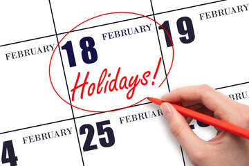 Hand drawing a red circle and writing the text Holidays on the calendar date 18 February. Important date.