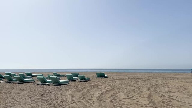Sunny summer day at the beach. Empty sun chairs and sun loungers with view of the blue ocean. Footage made at beach in Costa del Sol, outside Marbella in Spain.