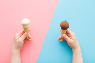 Baby girl or boy hands holding waffle cones of black chocolate and white vanilla ice cream on pink...