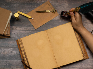 woman's hands, person dipping the pen in ink to write in an old, thick-eyed, yellowish notebook or...