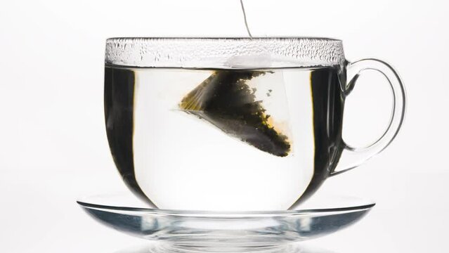 Tea Pyramid Sinks into the Cup. A tea bag in the form of a pyramid falls into a glass mug of hot water and stains it