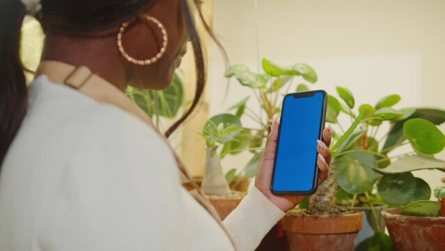 Forist African American woman holding phone with chroma key. Greenhouse worker female botanist, small business owner. Gardener working in flower shop, plant store. 