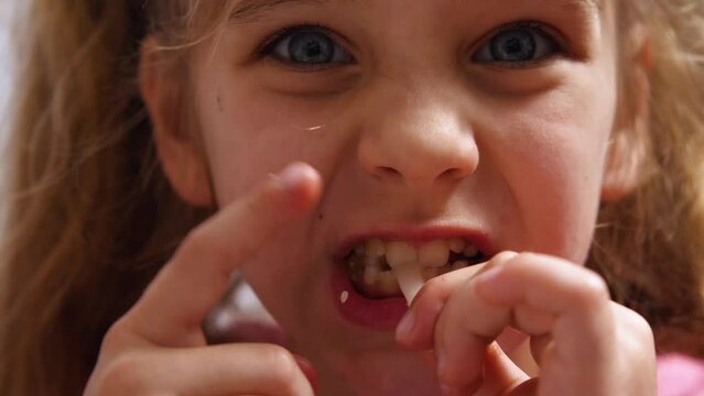 Close-up of a cute, funny child girl with big eyes eating squid rings. The girl's mouth is stained with sesame seeds. The girl is playing with the food